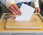Eine Hand steckt einen Zettel in eine Wahlurne ein