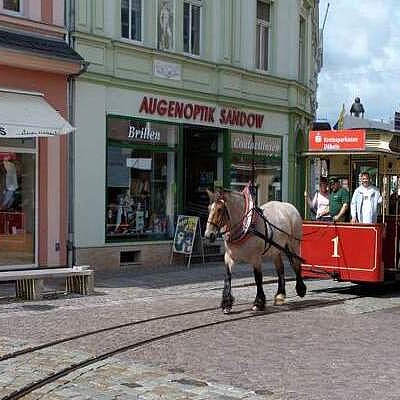 Der Wagen einer Straßenbahn wird von Pferden durch die Straßen gezogen