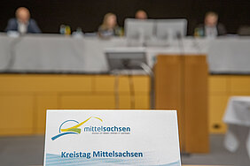 Tischkarte mit der Aufschrift Kreistag Mittelsachsen - im Hintergrund blick ins Gremium