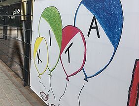 Wandbild mit gemalten Luftballons und Schriftzug Kita