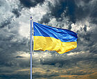 Dunkle Wolken am Himmel, davor weht die ukrainische Flagge