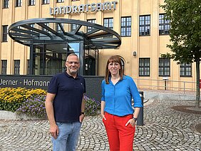 Landrat Dirk Neubauer (l.) & Demokratieministerin Katja Meier stehen vor dem Landratsamt in Freiberg und lächeln in die Kamera.