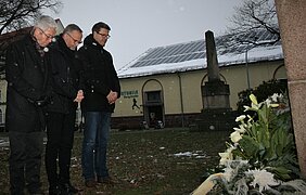 Drei Männer stehen vor einem Blumengebinde und gedenken den Verstorbenen