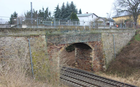 Eine Gewölbebrücke über einer zweigleisigen Bahnstrecke mit Bauzäunen gesichert