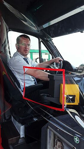 Ein Busfahrer sitzt am Steuer. Er ist vom Fahrgastraum durch eine Plastikfolie geschützt, diese hat ein Loch mit einer roten Umrandung um Fahrkarten zu verkaufen.