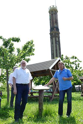 Zwei Männer stehen auf einer Wiese, im Hintergrund ein Aussichtsturm