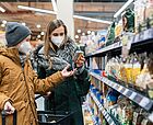Eine Frau mit FFP2-Maske ist mit einem Jungen im Supermarkt vorm Regal und schaut Produkte an