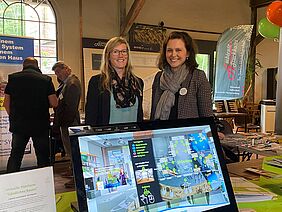 Zwei Frauen hinter einem Bildschirm, der einen Grundriss abbildet.